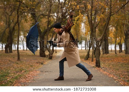Man with blue umbrella caught in gust of wind outdoors Royalty-Free Stock Photo #1872731008