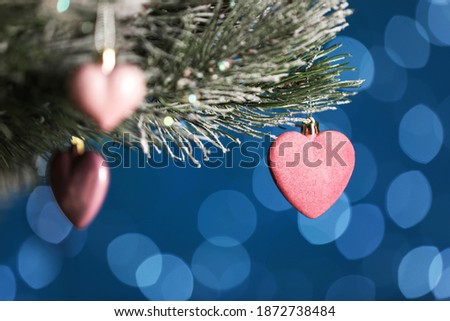 Beautiful holiday heart shaped bauble hanging on Christmas tree against blue background with blurred festive lights