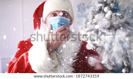 Real Santa Claus and christmas tree on a background, wearing a protective mask, glasses and hat. Christmas with social distance.
