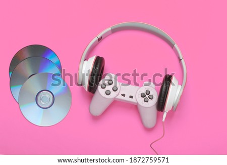 Stereo headphones with gamepad, cd discs on pink background. Gaming, leisure and entertainment concept. Top view.