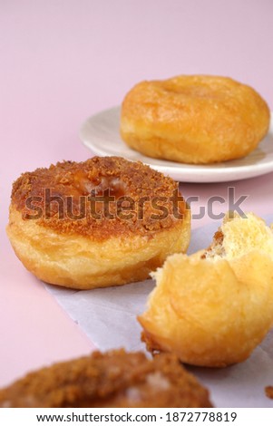 Grainy Donat or Donut or Doughnut with caramel and Lotus biscuit crumbs,. Selective focus, pink pastel background
