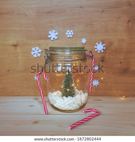 View of a jar filled with white capsules with a Christmas tree  with lights and snowflakes decorations on a warm wooden background. Medical background, medication background or pharmacy Christmas.