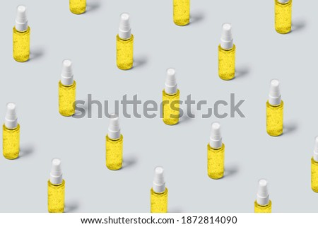 Pattern of bottles with yellow filling on gray background. Advertising cosmetics in the trendy colors of the new year.