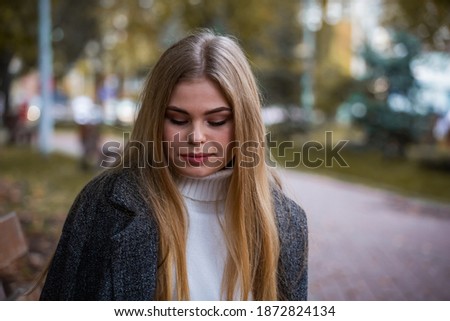 Blonde girl in autumn park sits on bench