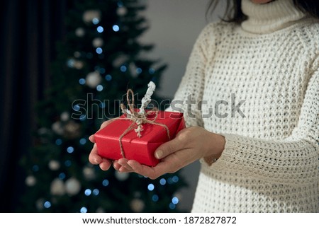 Close up shot of female hands holding a red and white gift wrapped with twine. The focus is on the box, on bokeh effect background. A present to Christmas, birthday, Valentine's Day and anniversary.