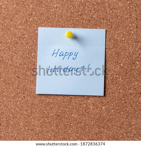 Happy holidays. Blue square sticker with writing in blue gel pen and pinned on corkboard. Winter holidays wishes.