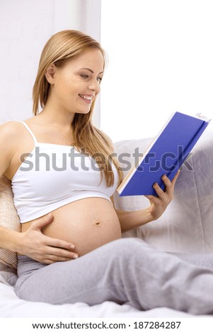 pregnancy and motherhood concept - smiling pregnant woman sitting on sofa and reading book at home