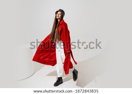 Fashion studio photo of stylish european brunette woman in red coat and black hat posing on white background.  Trendy winter accsesorises. Full lenght. 