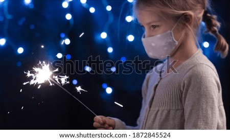 Little girl holding sparkler in the dark with face mask for new year and christmas.