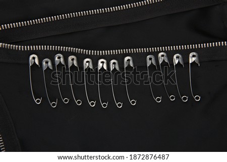 Safety pins and zippers on black fabric. Close up of subculture clothing. Royalty-Free Stock Photo #1872876487