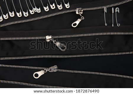 Safety pins and zippers on black fabric. Close up of subculture clothing.