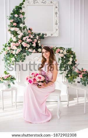 beautiful pregnant woman in a light pink dress in a light Studio with flowers