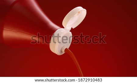 Ketchup, tomato sauce isolated on red background. Stock footage. Close up of ketchup pouring out of plastic bottle with white lid, concept of food preparation.
