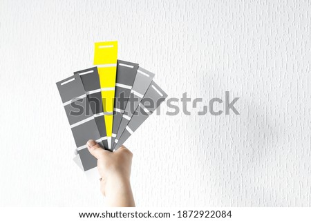 What color in 2021 will you choose? Trendy pantone colors on palette - Illuminating Yellow and Ultimate Gray. Holding color swatch guide in hand
