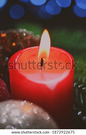 Red candle surrounded by holiday decorations.