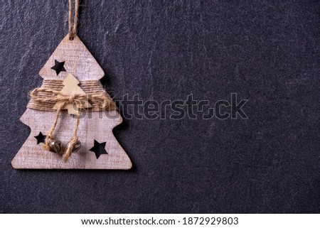 Craft handmade wooden Christmas toy placed left on dark grey background with copy space. Beautiful Christmas decoration. Christmas tree decorated with twine and bells.