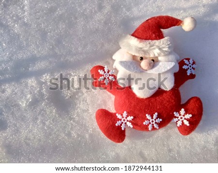 
santa toy in red clothes with white snowflakes on the background of shadows on the snow