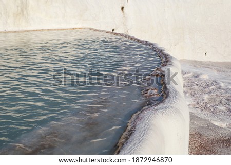 Blue turbid water in white travertine pool. Pure colors, no people. Sunset time. Unesco world heritage, famous Pamukkale, Turkey.