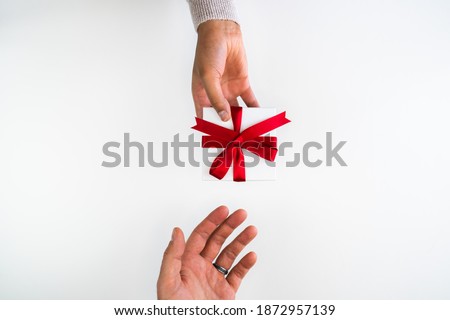 Beautiful holiday or Christmas background image of a mixed race African American woman handing a small red ribbon wrapped gift box to a Caucasian male's open hand on a white backdrop with copy space.
