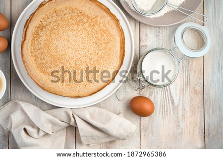 Pancakes on a flat white plate, egg, sugar and napkin on a light background. Top view, with space for writing. The concept of cooking, Mardi Gras.