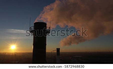 Air polluting industrial smoke stacks on sunset background in urban residential area, aerial view