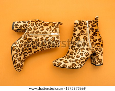 Top view shot of female boots with high heels and animal print on marigold orange backdrop. Colour trends of the year 2021. Spring summer trendy colours concept.