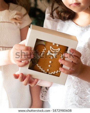 Small girls holding a white box with the gingerbread man in it, dressed in white dresses. Cropped picture.