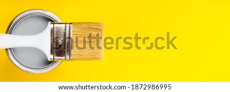 Banner made with open can of gray paint with white brush on it on yellow background. Top view. Repairing concept. Demonstrating colors of year 2021 - Gray and Yellow Royalty-Free Stock Photo #1872986995