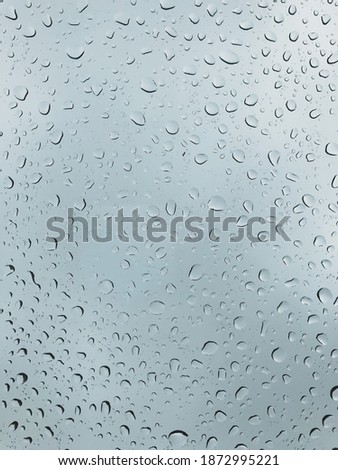 Selective focus of raindrops on window glasses surface with cloudy background. Natural pattern of raindrops isolated on cloudy background. Image may contain blurry and noise texture.
