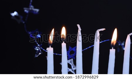 Close of Chanukah candles with shamash and two lights lit and Star of David decorations in the background
