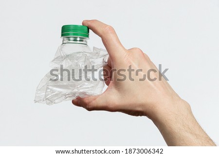 Hand holding smashed empty plastic bottle isolated on a white background