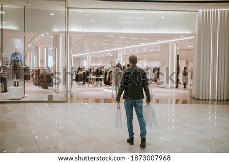 A picture from behind of a guy holding bags in his hands and entering a boutique