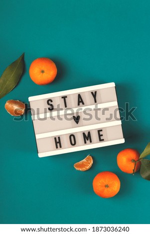 Stay Home written on lightbox among tangerines with green leaves. Christmas pandemic concept layout
