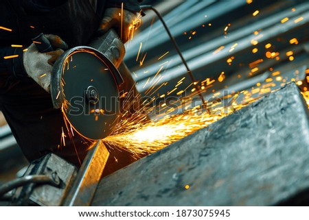 Cutting a metal beam using an angle grinder. A lot of sparks fly out from under the disk.