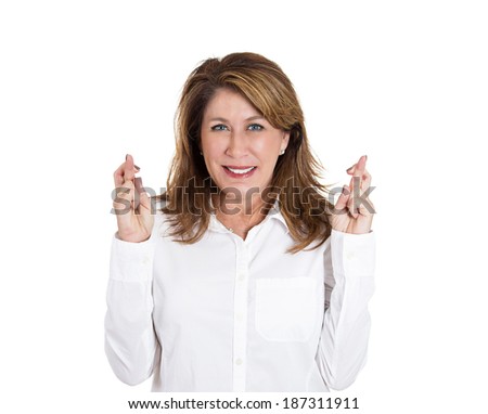 Closeup portrait, mature woman, crossing fingers, hoping for best future, looking at you, camera, in anticipation of life changer, isolated white background. Human emotion, facial expression, signs