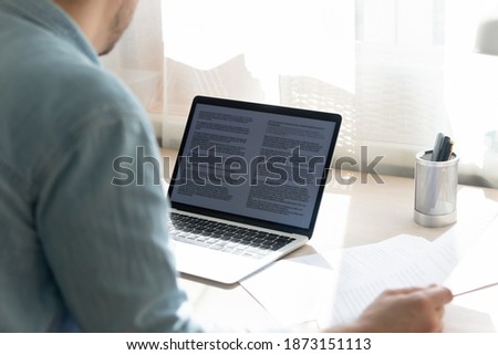 Close up young businessman working on research project, checking documents, holding paper sheet, looking at laptop screen, student writing diploma, essay, sitting at work desk, home office Royalty-Free Stock Photo #1873151113