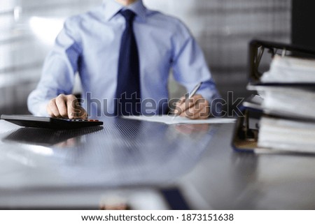 Unknown man accountant in blue shirt use calculator and computer with holding pen on while staying at home during covid pandemic. Taxes and audit concept