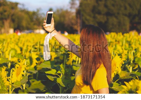 A women are taking picture with sunflower field, holding smartphone in hands and taking selfie. Travel on the weekend concept