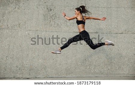 Female athlete running and jumping. Side view of flexible female athlete exercising outdoors. Royalty-Free Stock Photo #1873179118