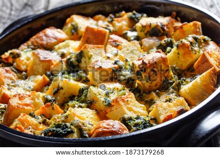 Italian spinach strata of soaked overnight cubed sandwich bread and baked with chopped spinach and shredded cheese with mustard served on a black baking dish on a wooden background, top view Royalty-Free Stock Photo #1873179268