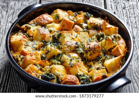 Italian spinach strata of soaked overnight cubed sandwich bread and baked with chopped spinach and shredded cheese with mustard served on a black baking dish on a wooden background, top view Royalty-Free Stock Photo #1873179277