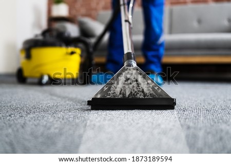 Janitor Cleaning Carpet With Vacuum Cleaner At Home Royalty-Free Stock Photo #1873189594