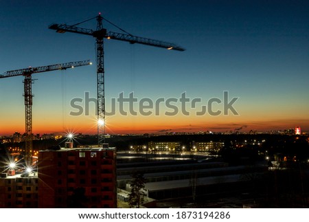 Two construction building cranes over cityscape at evening or night with lights of city.