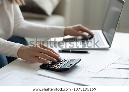 Close up young woman using calculator and laptop, checking domestic bills, sitting at table with financial documents, managing planning budget, accounting expenses, browsing internet service Royalty-Free Stock Photo #1873195159