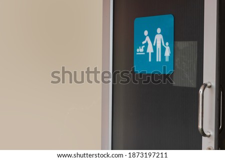 Image of family restroom sign shown on slide door of public toilet with clear light brown coloring wall for copy space background. 