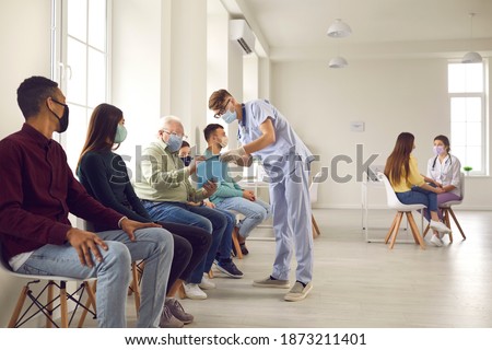 Diverse people waiting in line to get shots or to get tested for Covid-19 infection at the hospital. Senior patient signing Informed Consent for Vaccination against pneumonia, influenza or coronavirus Royalty-Free Stock Photo #1873211401