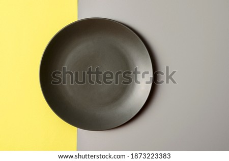 A grey plate on grey and yellow background. Trendy colors of 2021 - grey and yellow