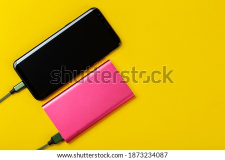 Smartphone Charging with Power Bank on Yelloy Background. Space for text. Top View.
