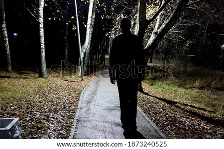 Silhouette of a tall man in the park at night. Lantern and man. Dangerous situation in the park