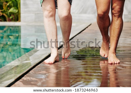 Cropped image of husband and wife walking along wet wooden edge of swimming pool in spa hotel